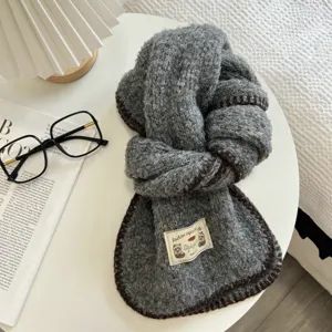 Close up detail of grey fluffy knit scarf with dark brown lock edge on white table view.