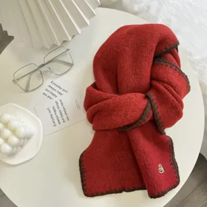Close-up of red knitted winter scarf with brown contrast stitch edge and detail charm setup.