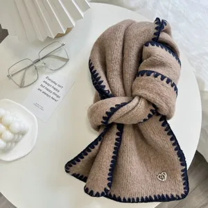Detailed view of winter knitted scarf with contrast stitching and heart charm on white table.