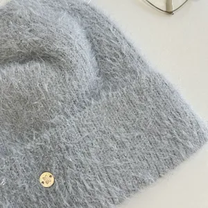 Grey fuzzy knit beanie hat detail view, soft plush texture with a small metallic logo tag.