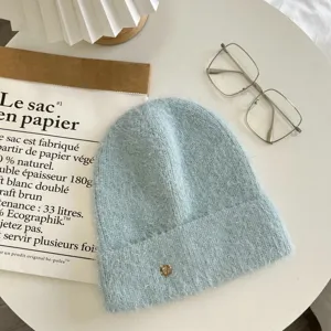Detailed close-up shot of a light blue fuzzy knitted beanie hat with a small metal charm.