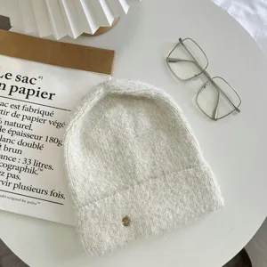 Cozy knitted beanie hat with metallic logo detail, soft winter warm wool cap, detail view.