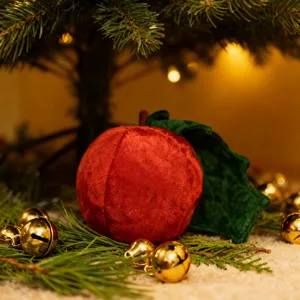 Nahaufnahme vom roten Plüsch-Apfelspielzeug mit grünem Blatt unter weihnachtlicher Tannenbaum-Deko.
