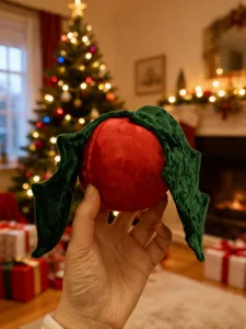 Nahaufnahme von niedlichem roten Plüsch-Weihnachtsornament mit grünen Samt-Blättern, Festtagsdeko.