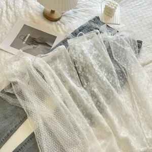 Dettagli della gonna a strati in pizzo bianco trasparente abbinata ai jeans per stile chic.