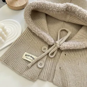 Detail shot of beige knitted hooded shawl with plush trim, drawstring, and button accents.