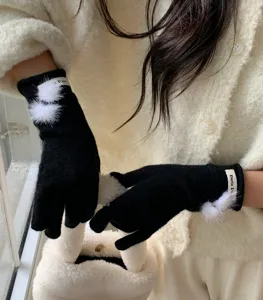 Detailopname van zwarte gebreide winterhandschoenen met donzige witte pompons en polsetiket.