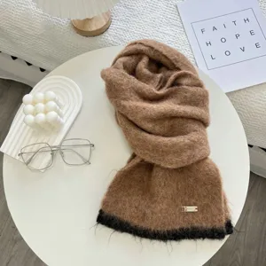 Détail d'écharpe en tricot avec texture marron douce, bord noir élégant et étiquette métal.