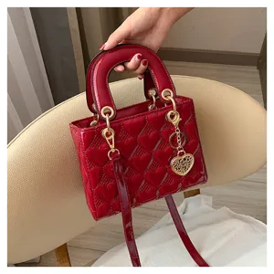 Red patent leather heart quilted handbag with top handle and stylish metal chain charm detail.