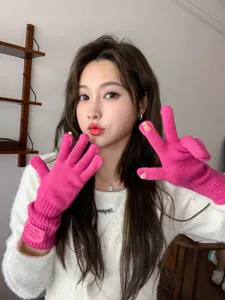 Close-up detail of bright pink knitted arm warmer gloves with split fingers and wrist label.