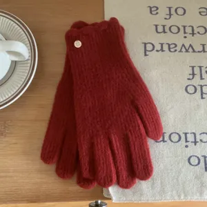 Gros plan de gants tricotés rouges avec volants et bouton en métal sur fond bois.