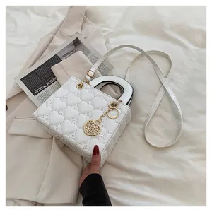 White patent leather handbag detail featuring quilted heart patterns and a gold charm on bed.