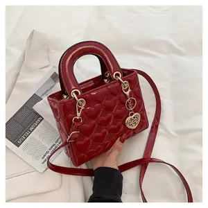 Red patent leather quilted heart handbag detail, elegant top handle crossbody bag close-up.