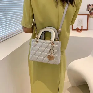 Chic white heart quilted crossbody bag with top handle and elegant golden heart charm.