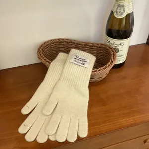 Close up of beige knitted long gloves with woven label, cozy winter accessory detail.