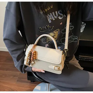 Detail view of stylish small square handbag with beaded charm and elegant leather strap.