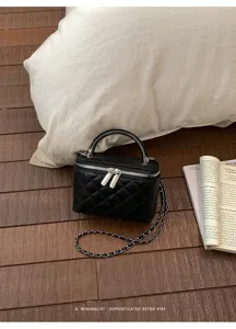 Detailed shot of black quilted vanity bag with metal handle and chain strap on wood floor.