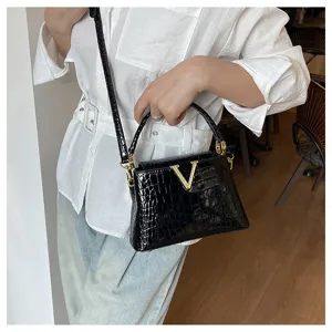 Close-up detail of black crocodile embossed shoulder bag with luxury golden V-shaped rhinestone clasp.