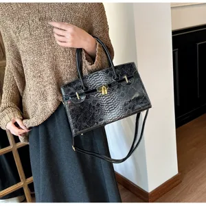 Detailansicht einer schwarzen Handtasche mit Schlangenmuster, goldenen Beschlägen.