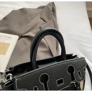 Black leather top handle shoulder bag with contrast white stitching and classic flap design.