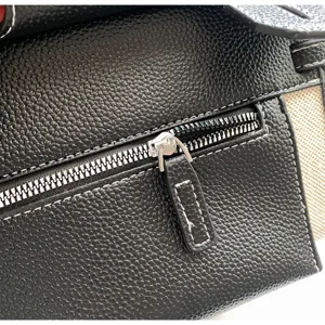 Detailed view of women's black textured leather and canvas handbag with metal zipper and stitching.