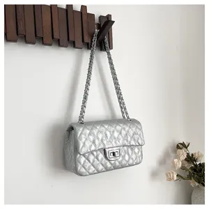 Detail shot of the silver quilted shoulder bag hanging on wooden wall hook with elegant chain.