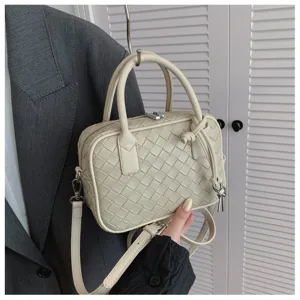 Detailed view of beige woven leather crossbody bag with top handles and adjustable shoulder strap.
