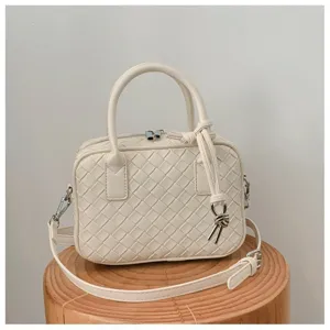 Close-up detail of cream woven leather handbag with stylish knot strap and double top handles.