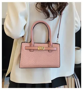 Detail view of pink woven texture handbag with golden turn-lock clasp and shoulder strap.