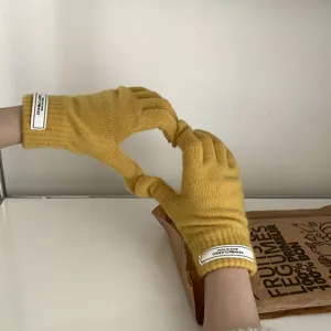 Primer plano de guantes de punto amarillo liso táctiles con elegante etiqueta en el puño, detalle.