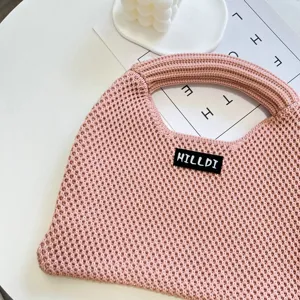 Nahaufnahme der stilvollen rosa Strickhandtasche mit feiner Textur und Markenetikett.