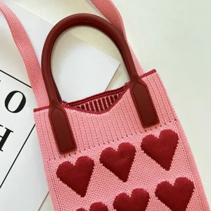 Nahaufnahme der rosagehäkelten Mini-Handytasche mit rotem Herzmuster und Silikongriff.