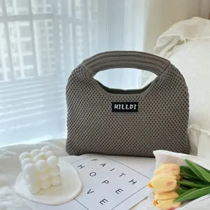 Nahaufnahme einer grauen Strickhandtasche mit strukturierter Webung und Etikett im Wohnstil.