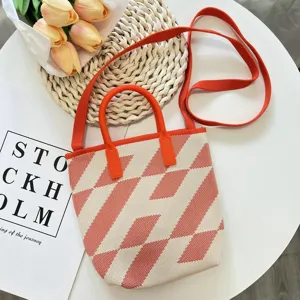 Gestrickte geometrische Tasche mit roten Griffen und Schulterriemen, stilvolles Detail.