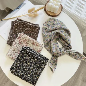 Détail du petit foulard floral en coton et lin avec bord de perles délicat sur table.