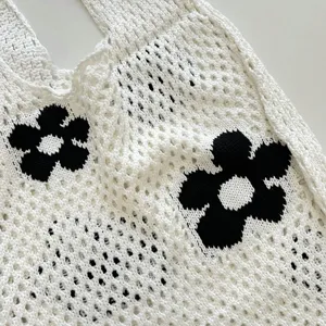 Close-up detail of white knit crochet tote bag featuring trendy black flower pattern.