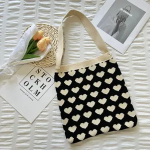 Gros plan détaillé du sac cabas en tricot cœur noir et blanc dans un décor plat esthétique.