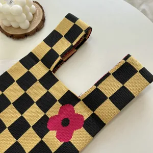 Knit tote bag detail, black yellow checkerboard pattern with pink flower, stylish knitwear.