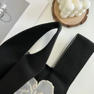 Gros plan détail d'un sac cabas en tricot noir avec un motif de cœur contrasté.