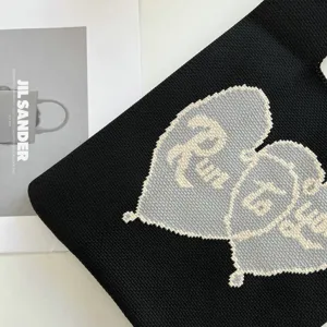 Gros plan détaillé d'un sac cabas en tricot noir avec motif de cœur contrasté et texte.
