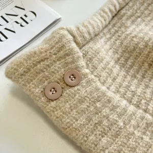 Nahaufnahme der kuscheligen, beigen Strickmütze mit süßen pinken Knöpfen und weichem Stoff.