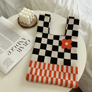 Chic knitted tote bag with black white checkerboard pattern and orange flower detail.