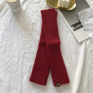 Detail view of red knitted half-finger sleeves, cozy ribbed winter arm warmers with patch label.