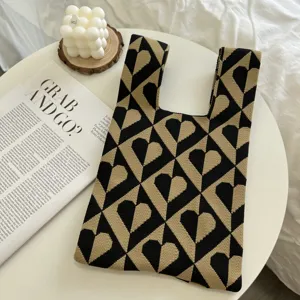 Detail shot of the black and beige knitted heart pattern tote bag on a styled table.