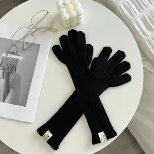 Black knit long gloves detail view, warm winter five-finger gloves on white table scene.