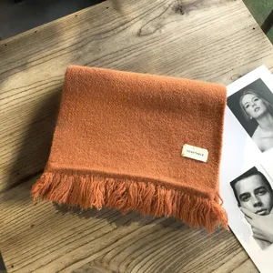 Oranger geflochtener Winterschal mit Fransen und Etikett, gemütliches Kaltwetter-Accessoire.