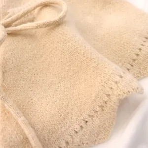 Close-up detail of beige knitted shawl, featuring soft texture and drawstring tie.