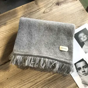 Gemütlicher grauer Strickschal für den Winter mit Fransen und stylischem Etikett.
