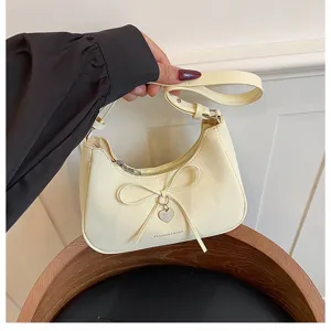 Vue détaillée du sac porté épaule crème avec un élégant nœud et un charmant pendentif.
