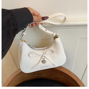 Vue détaillée du sac à bandoulière croissant blanc avec un nœud et pendentif cœur.